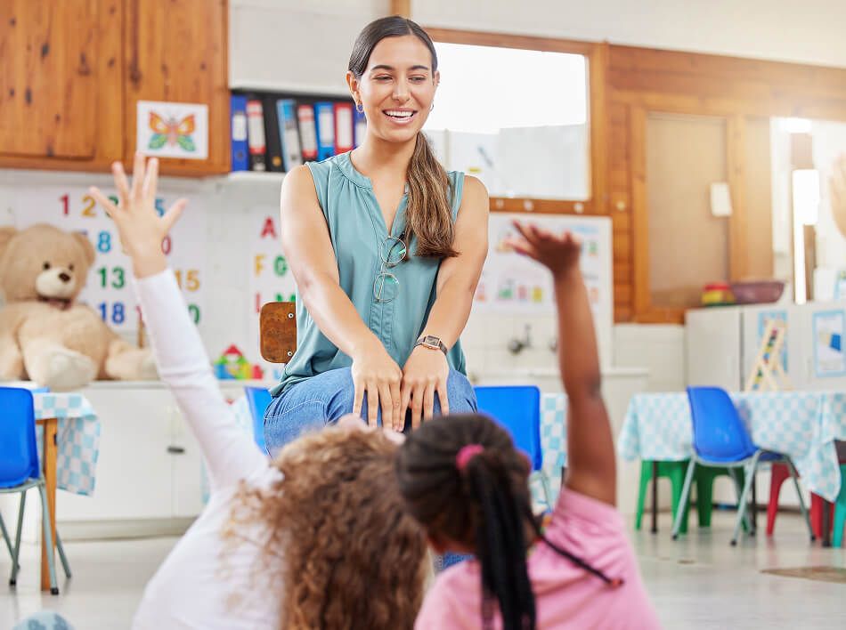 Woman Teacher smiling at two children raising their hands