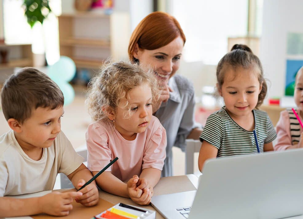 Teacher sitting with toddlers in front of a computer